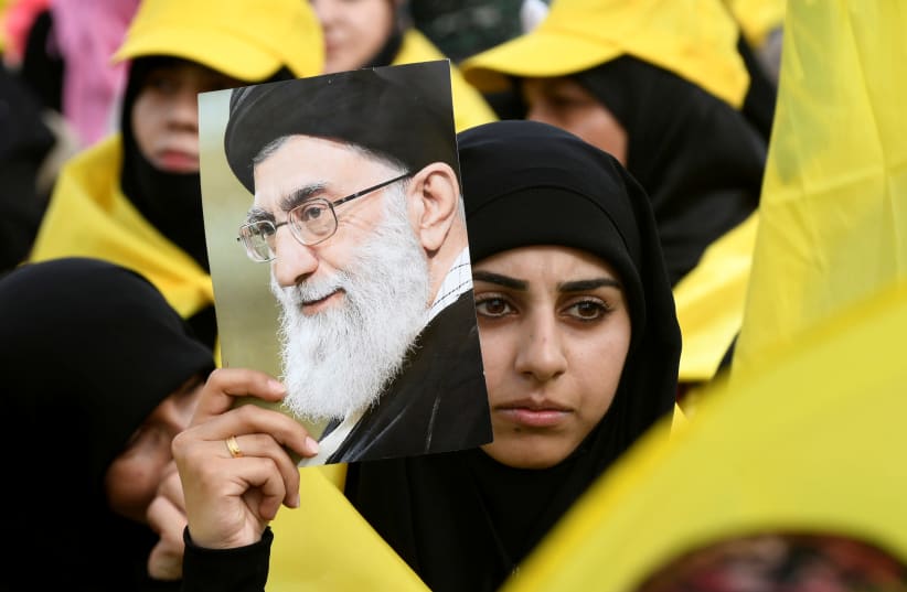 A woman carries a picture of Iran's Supreme Leader Ayatollah Ali Khamenei as she watches Lebanon's Hezbollah leader Sayyed Hassan Nasrallah appear on a screen during a live broadcast to speak to his supporters at an event marking Resistance and Liberation Day in the Bekaa Valley, Lebanon, May 25, 20 (photo credit: HASSAN ABDALLAH / REUTERS)