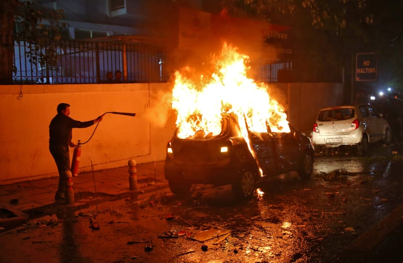 A man tries to extinguish a burning car after demonstrators set it on fire during a protest against a new citizenship law, in New Delhi (photo credit: REUTERS)