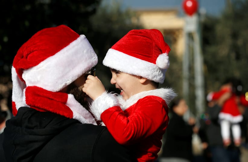 A man plays with his kid in a street before the beginning of an annual "Christmas Run" in Mi'ilya, a Christian Arab village in northern Israel December 21, 2018 (photo credit: RONEN ZVULUN/REUTERS)