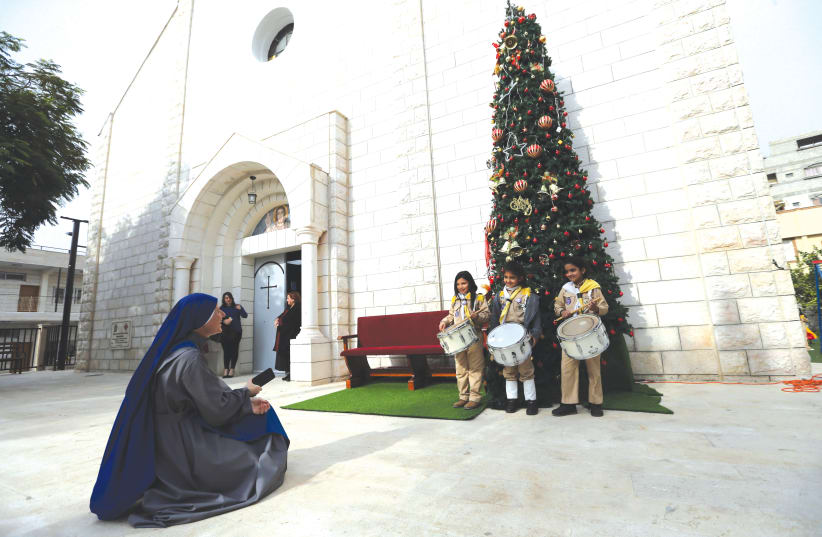 PALESTINIAN GIRL scouts pose for a photo in front of a Christmas tree outside the Holy Family Church in Gaza City.  (photo credit: REUTERS)