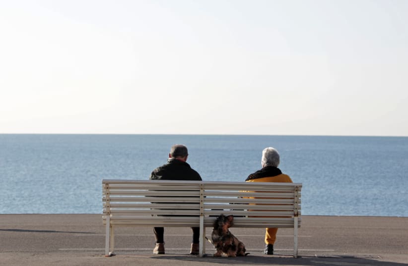 Elderly people sit on a bench to take in the sun along the Promenade Des Anglais in Nice (photo credit: ERIC GAILLARD/REUTERS)