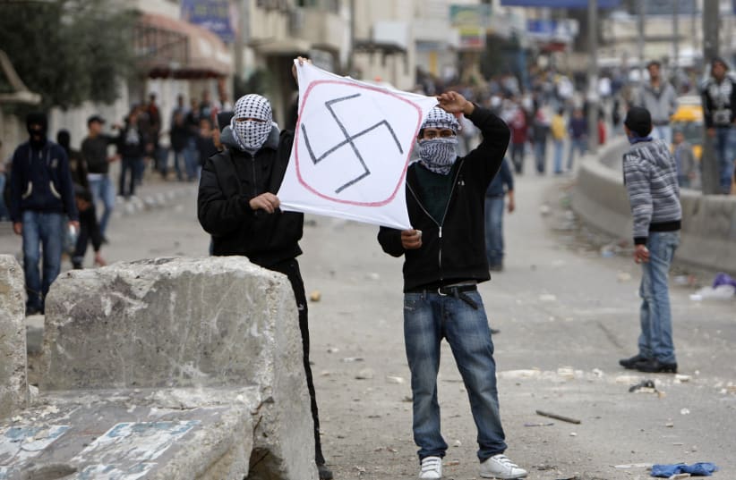 Palestinian protesters hold up a swastika in an anti-Israel protest in the West Bank. (photo credit: REUTERS)