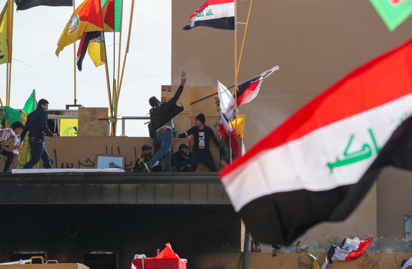 Protesters and militia fighters throw stones towards the U.S. Embassy during a protest to condemn air strikes on bases belonging to Hashd al-Shaabi (paramilitary forces), outside the U.S. Embassy in Baghdad, Iraq January 1, 2020. (photo credit: REUTERS/THAIER AL-SUDANI)
