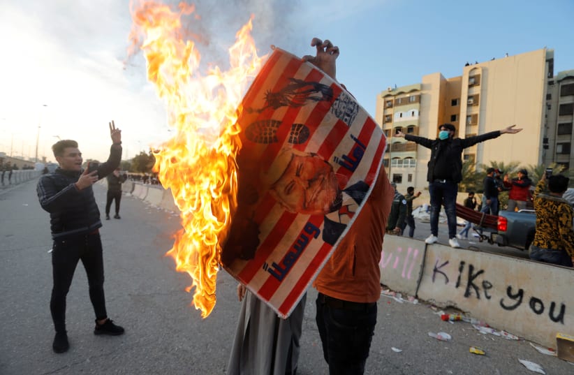 A protester holds a placard with U.S. President Donald Trump illustration burning outside the U.S. Embassy during a protest to condemn air strikes on bases belonging to Hashd al-Shaabi (paramilitary forces), in Baghdad, Iraq January 1, 2020 (photo credit: REUTERS/KHALID AL MOUSILY)