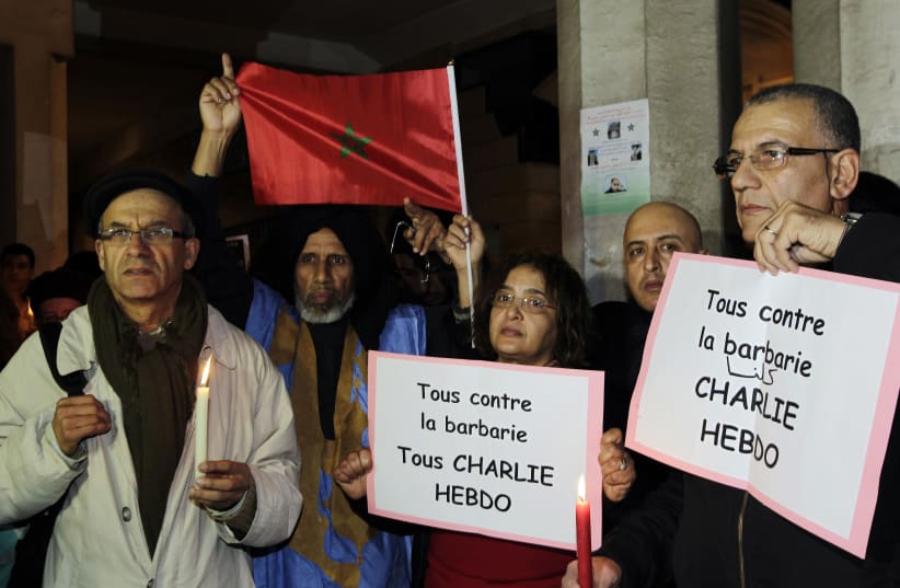 People hold cards that read "We are all against barbarism, we are Charlie Hedbo" to pay tribute to the victims of a shooting by gunmen at the offices of French weekly newspaper Charlie Hebdo in Paris, during a memorial ceremony in Rabat (photo credit: REUTERS)