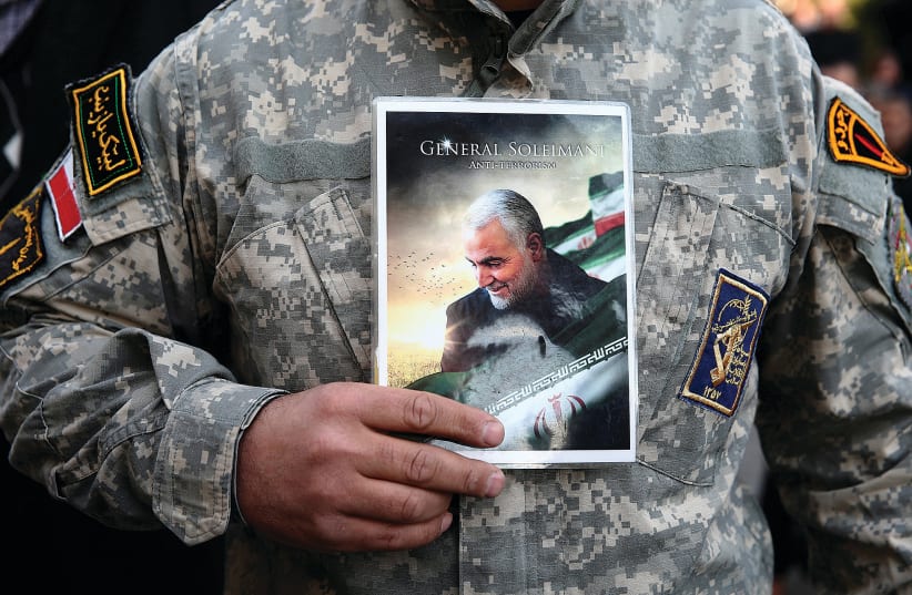 A man in uniform holds a picture of Qasem Soleimani during a protest in Tehran following his targeted assassination.  (photo credit: NAZANIN TABATABAEE/WANA VIA REUTERS)