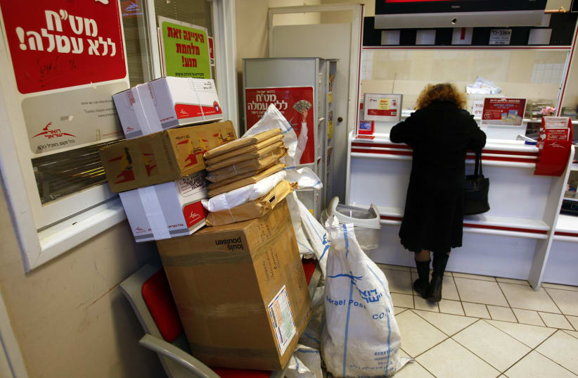 A woman stands at the counter inside a Israel Post office in Jerusalem (photo credit: REUTERS/Ronen Zvulun)