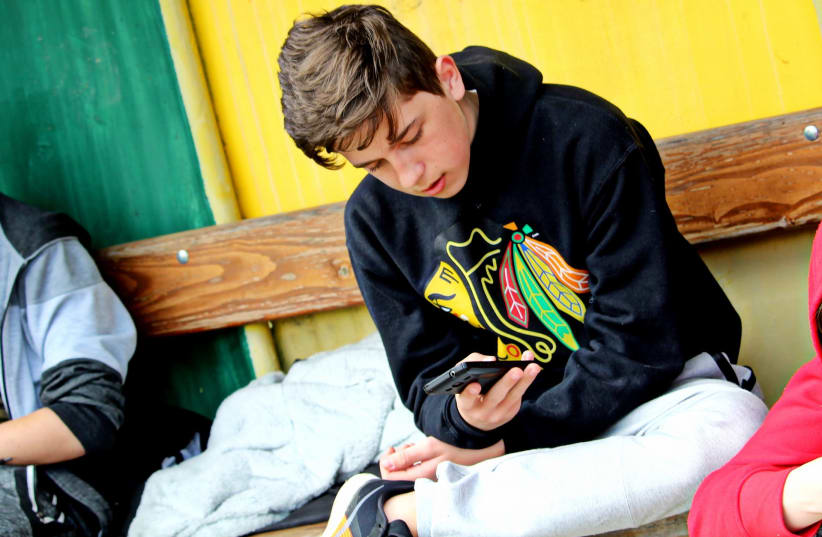 A teenage boy looks at his smartphone screen.  (photo credit: CREATIVE COMMONS)