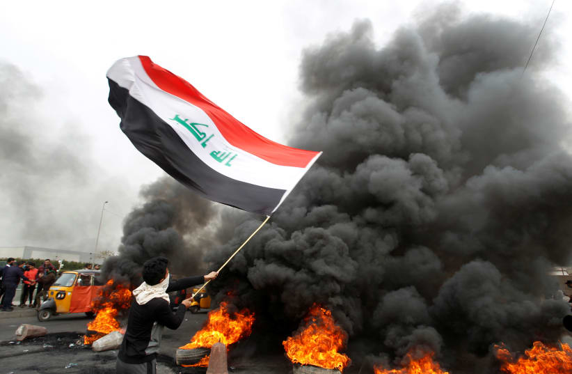 A demonstrator carries an Iraqi flag as he walks near burning tires blocking a road during ongoing anti-government protests, in Baghdad, Iraq January 19, 2020. (photo credit: KHALID AL MOUSILY / REUTERS)