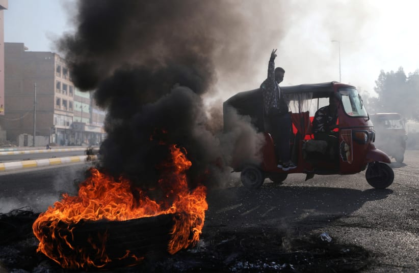 A tuk-tuk drives next to burning tires blocking a road, during ongoing anti-government protests, in Kerbala, Iraq January 20, 2020 (photo credit: REUTERS/ABDULLAH DHIAA AL-DEEN)
