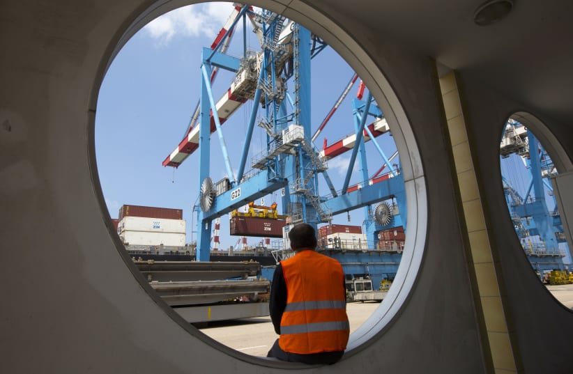 A worker sits as a crane unloads containers from a ship at the port of Haifa (photo credit: REUTERS)