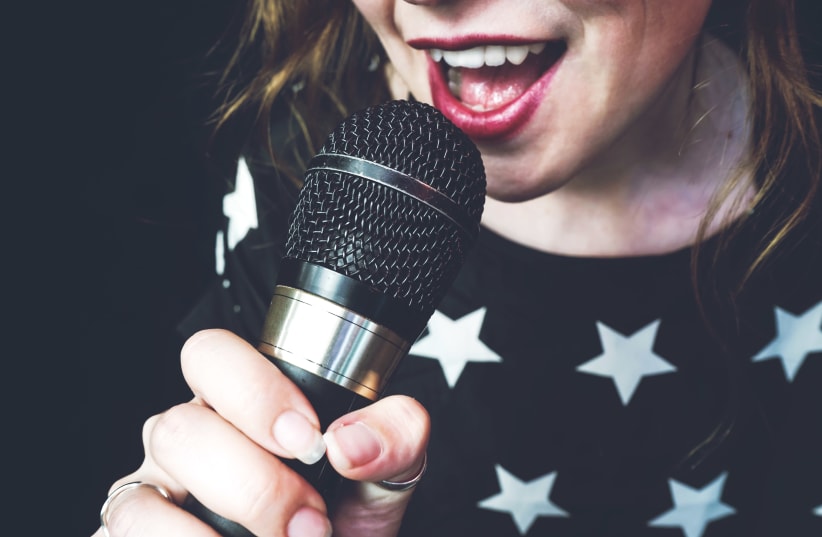 Young woman singing a song with a microphone (photo credit: INGIMAGE)