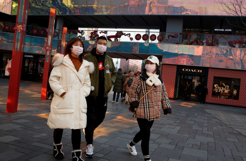 People wearing face masks walk past luxury boutiques in the Sanlitun shopping district in Beijing, China, as the country is hit by an outbreak of the new coronavirus, January 25, 2020 (photo credit: REUTERS/THOMAS PETER)