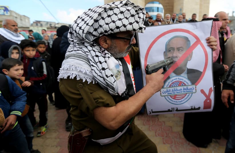 A Palestinian demonstrator points a toy gun on a poster depicting Israeli Prime Minister Benjamin Netanyahu during a protest against the U.S. Middle East peace plan, in Rafah in the southern Gaza Strip January 28, 2020 (photo credit: REUTERS/IBRAHEEM ABU MUSTAFA)