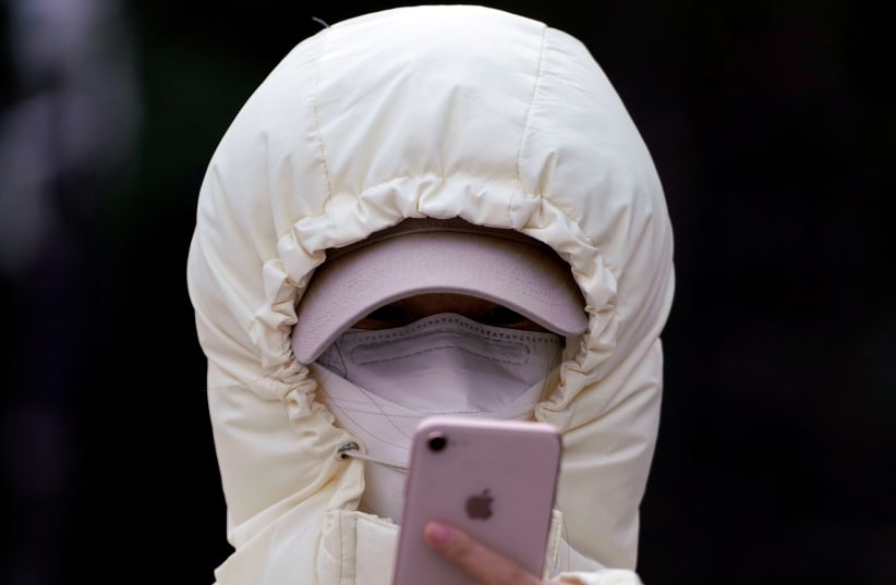 A woman wearing a mask checks her mobile phone in Shanghai, China January 29, 2020 (photo credit: REUTERS/ALY SONG)