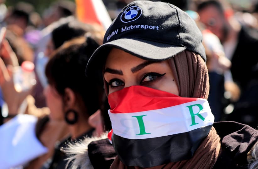 An Iraqi university student covers her face with Iraqi flag as she protests to express her rejection of the newly appointed Prime Minister of Iraq, Mohammed Tawfiq Allawi, during ongoing anti-government protests in Baghdad (photo credit: REUTERS)
