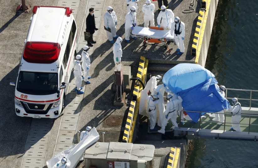Officers in protective gear escort a person who was on board cruise ship Diamond Princess and was tested positive for coronavirus, after the person is transferred to a maritime police base in Yokohama (photo credit: REUTERS)