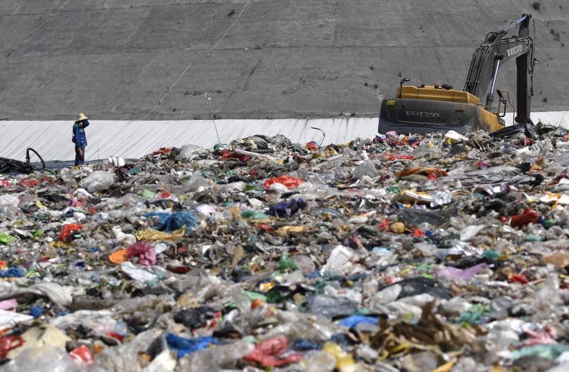 An environmental worker stands near an excavator amid waste at Tianziling landfill in Hangzhou, Zhejiang province, China August 7, 2019. (photo credit: REUTERS/STRINGER)