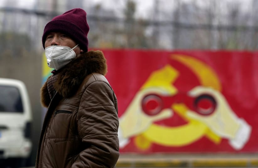 A man wears a mask as he walks past a mural showing a modified image of the Chinese Communist Party emblem in Shanghai, China after the country is hit by an outbreak of the new coronavirus, January 28, 2020 (photo credit: REUTERS/ALY SONG)