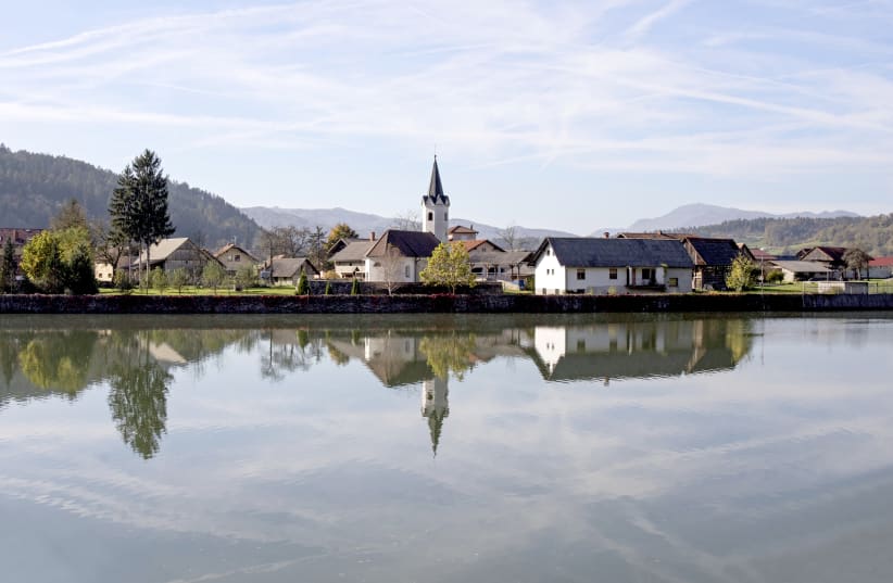 A CHURCH and houses in the small village of Kompolje, Slovenia reflect into the waters of the Sava River. This tranquil shot was actually taken from a fast-moving train. (photo credit: ILAN ROGERS)