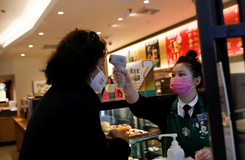 A worker uses a thermometer to check the temperature of a customer as she enters a Starbucks shop as the country is hit by an outbreak of the new coronavirus, in Beijing, China January 30, 2020. (photo credit: CARLOS GARCIA RAWLINS/ REUTERS)