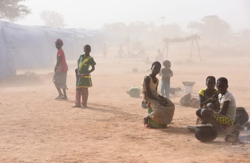 Displaced people, who fled from attacks of armed militants in Roffenega, are engulfed in dust as they sit at the camp built by the German Ngo HELP in Pissila (photo credit: REUTERS)