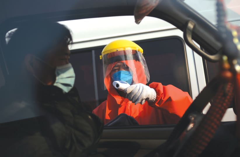 A WORKER in a protective suit checks temperature of a truck driver entering a wholesale market for agricultural products in Beijing. (photo credit: REUTERS)