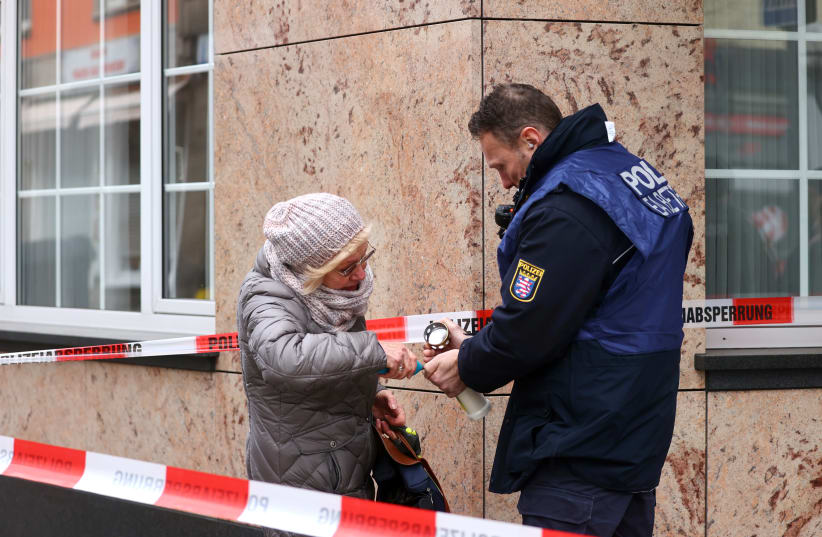 A police officer helps a woman to light a candle to place it on a makeshift memorial outside one of the crime scenes following a shooting in Hanau, near Frankfurt, Germany, February 20, 2020 (photo credit: REUTERS/KAI PFAFFENBACH)