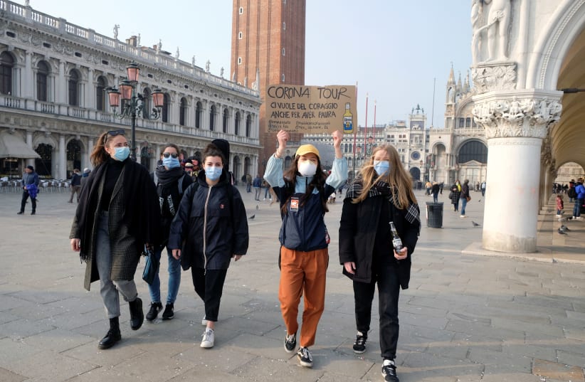 People wear protective face masks as they walk in St. Mark's square after the last days of Venice Carnival were cancelled due to coronavirus, in Venice (photo credit: REUTERS)