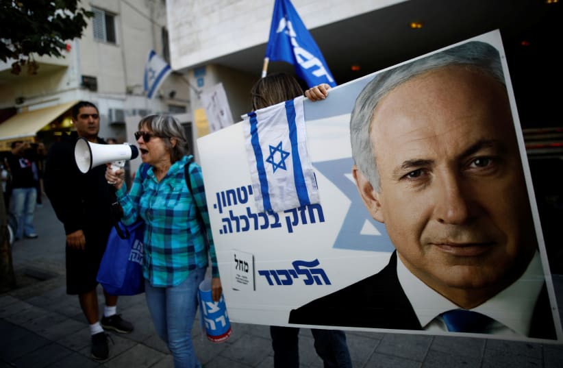 Supporters of Israeli Prime Minister Benjamin Netanyahu protest outside Likud Party headquarters in Tel Aviv, Israel November 22, 2019. The placards in Hebrew read, "Strong in security, strong in Economy  (photo credit: REUTERS/CORINNA KERN)