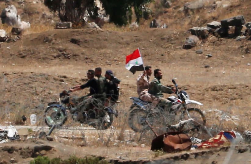 Uniformed men ride a motorbike as they carry a Syrian flag in Quneitra on the Syrian side of the ceasefire line between Israel and Syria, as seen from the Israeli-occupied Golan Heights (photo credit: REUTERS/AMMAR AWAD)