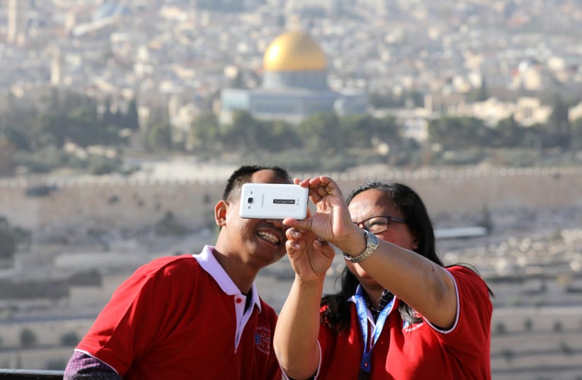 Tourists look at a mobile phone as they stand at an observation point overlooking the Dome of the Rock and Jerusalem's Old City (photo credit: REUTERS)