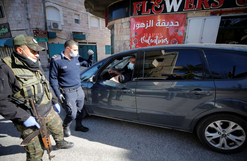 A policeman checks the identity card of a Palestinian entering to the city of Bethlehem amid coronavirus precautions (photo credit: MUSSA ISSA QAWASMA/REUTERS)