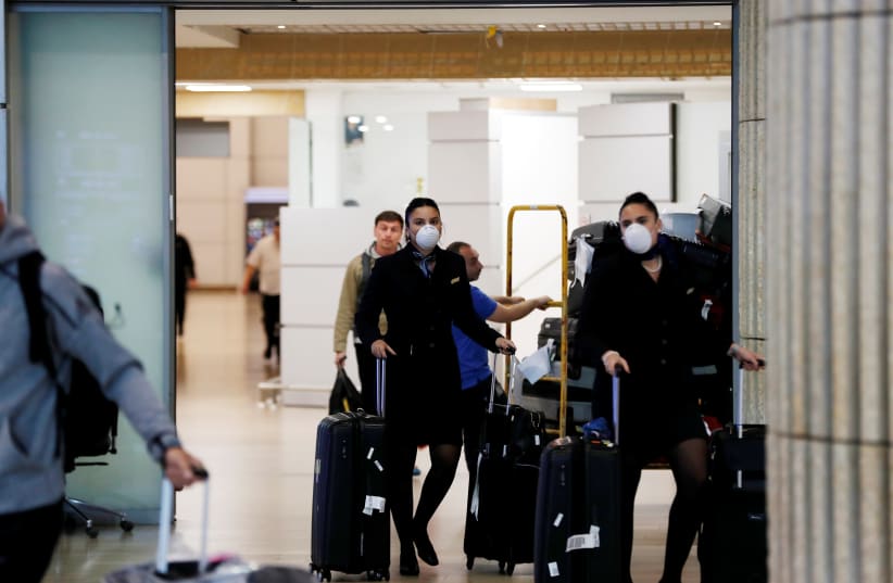 Airline employees wearing masks walk in the arrivals terminal after Israel said it will require anyone arriving from overseas to self-quarantine for 14 days as a precaution against the spread of coronavirus, at Ben Gurion International airport in Lod, near Tel Aviv, Israel March 10, 2020 (photo credit: REUTERS/RONEN ZEVULUN)