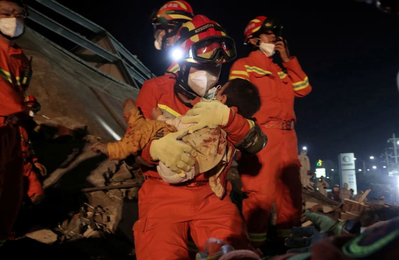 A worker wearing a face mask rescues a child at the site where a hotel being used for the coronavirus quarantine collapsed, in the southeast Chinese port city of Quanzhou, Fujian province, China March 8, 2020. (photo credit: CHINA DAILY VIA REUTERS)