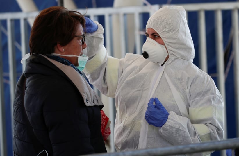 A person wearing a protective suit and mask checks the temperature of people departing from the ferry port of Molo Beverello after Italy orders a countrywide lockdown to try and contain a coronavirus outbreak, in Naples, Italy, March 10, 2020 (photo credit: REUTERS/CIRO DE LUCA)
