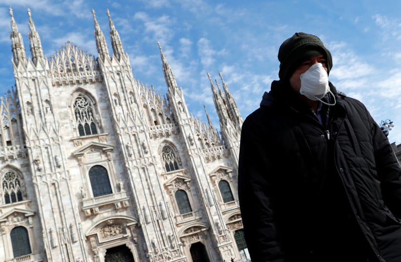 A man wearing a protective face mask to prevent contracting the coronavirus walks past the Duomo Cathedral in Milan, Italy, March 4, 2020 (photo credit: GUGLIELMO MANGIAPANE / REUTERS)