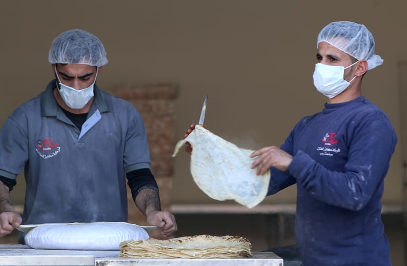 Palestinian workers, wearing masks amid coronavirus precautions, bake bread at a bakery in Gaza City March 8, 2020 (photo credit: REUTERS/MOHAMMED SALEM)