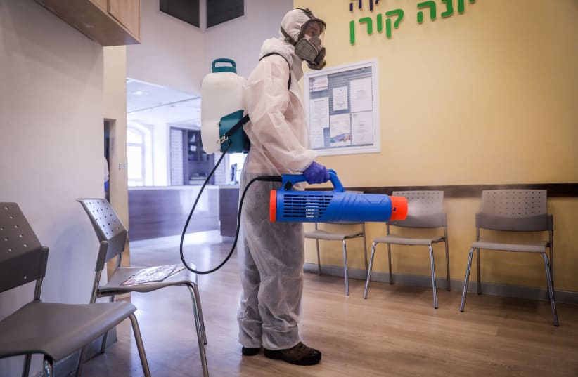 Workers wearing protective clothes disinfect a shop in Jerusalem, on March 15, 2020, as part of measures to prevent the spread of the Coronavirus. (photo credit: YONATAN SINDEL/FLASH90)