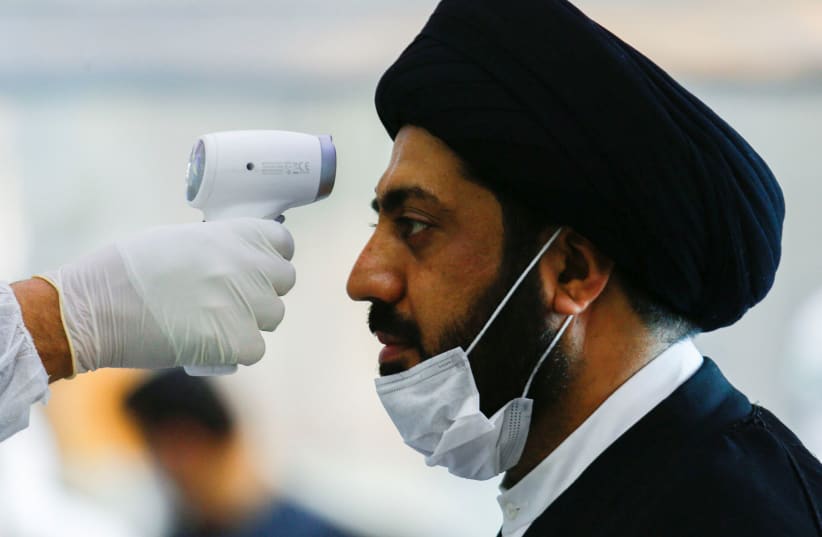 A medical staff member in protective gear checks the temperature of a cleric man amid concerns over the coronavirus (COVID-19) spread, at Najaf airport in the holy city of Najaf upon his arrival from Iran, Iraq March 15, 2020. (photo credit: REUTERS/ALAA AL-MARJANI)