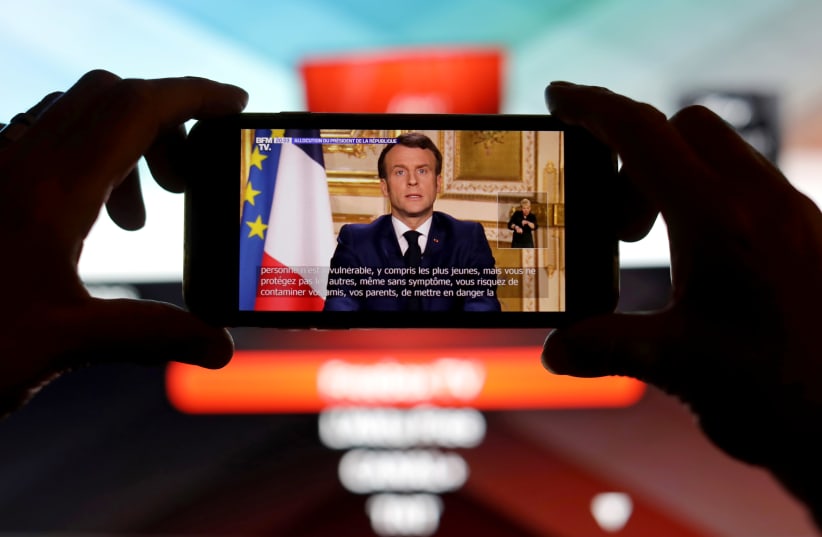 French President Emmanuel Macron is seen addresses the nation about the coronavirus disease (COVID-19) outbreak, on a mobile screen in this illustration picture (photo credit: REUTERS)