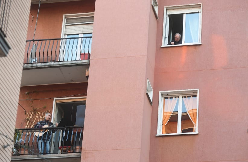 A man plays the guitar and sings from a balcony to raise morale on the sixth day of an unprecedented lockdown across of all Italy imposed to slow the outbreak of coronavirus in Milan, Italy March 15, 2020 (photo credit: DANIELE MASCOLO / REUTERS)
