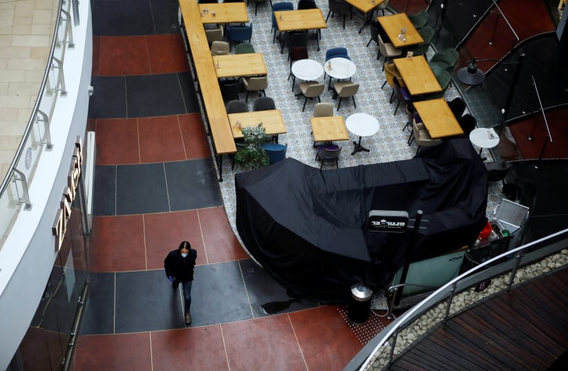 A man wearing a mask walks inside a shopping centre after Israeli Prime Minister Benjamin Netanyahu's government announced that malls, hotels, restaurants and theaters will shut down from Sunday, in an escalation of precautionary measures against coronavirus, in Tel Aviv, Israel March 15, 2020 (photo credit: REUTERS/NIR ELIAS)