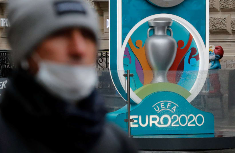 A person wearing a protective face mask walks past the Euro 2020 countdown clock in Saint Petersburg (photo credit: REUTERS)
