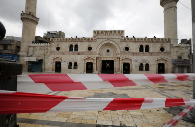 Plastic warning tape hangs in front of al Husseini mosque building after closing it to the worshippers amid concerns over the coronavirus disease (COVID-19) spread, in downtown Amman, Jordan, March 20, 2020.  (photo credit: REUTERS)