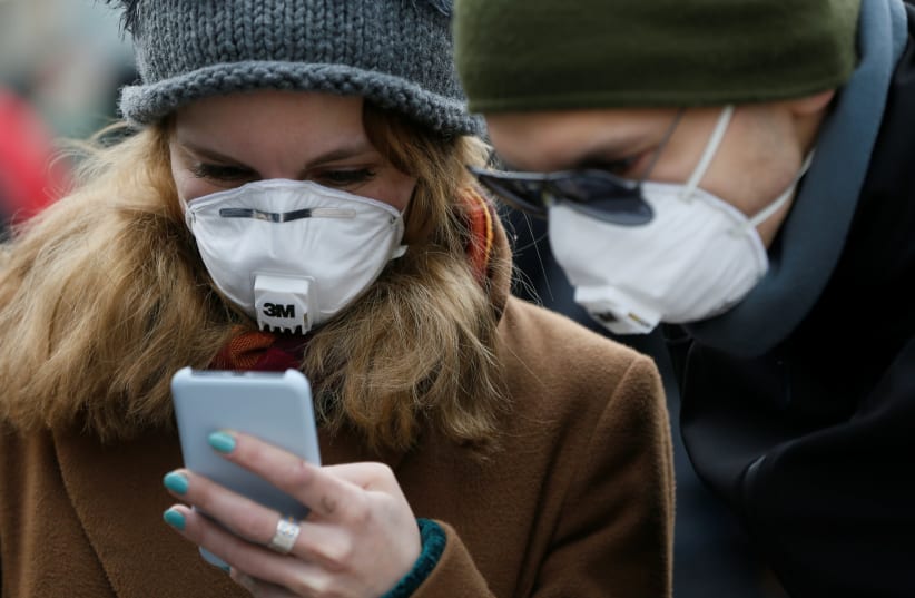 People wearing protective face masks use a smartphone on a street amid coronavirus (COVID-19) concerns (photo credit: REUTERS/VALENTYN OGIRENKO)