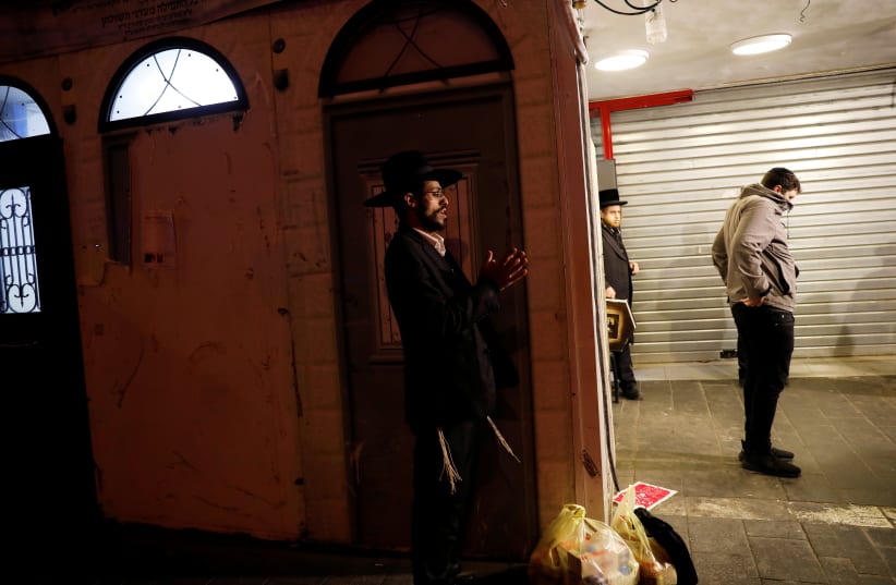 Ultra-Orthodox Jewish men pray next to a shuttered synagogue as Israelis were instructed on Wednesday to stay within 100 meters (110 yards) of their homes for a week under tightened restrictions to curb the coronavirus disease (COVID-19), in Mea Shearim neighborhood of Jerusalem March 25, 2020 (photo credit: REUTERS/Ronen Zvulun)
