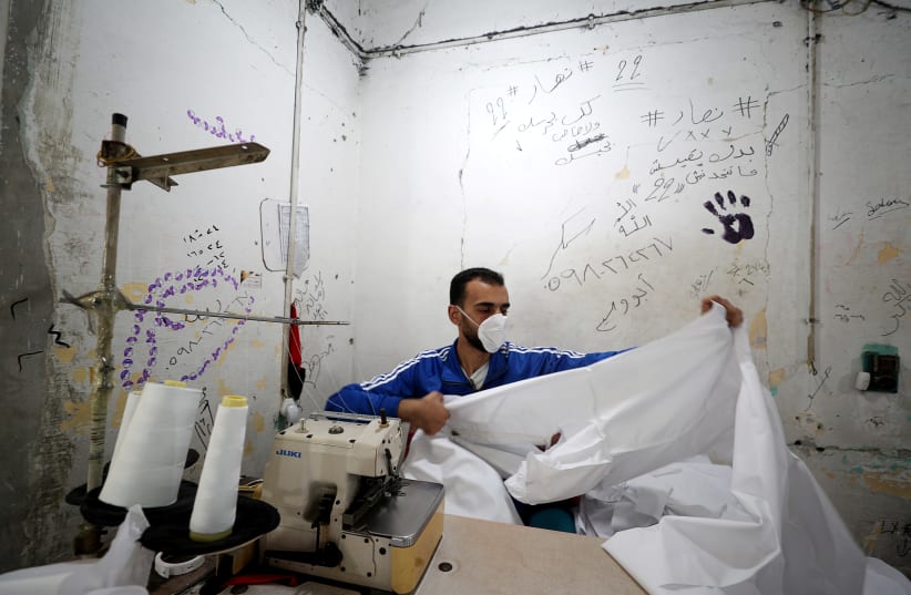 A Palestinian worker makes a protective suit at a factory amid concerns over the spread of the coronavirus disease (COVID-19), east of Gaza City March 29, 2020 (photo credit: REUTERS/MOHAMMED SALEM)