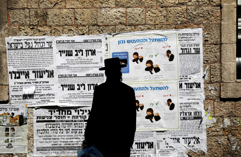 A Jewish ultra-Orthodox man looks onto a local billboard with instructions related to the coronavirus at a street in a Jewish Orthodox neighborhood in Jerusalem, March 27, 2020 (photo credit: REUTERS/Ronen Zvulun)