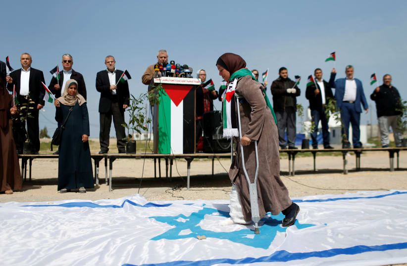 A Palestinian woman steps on a replica of an Israeli flag during an event marking Land Day near the Israel-Gaza border as mass rallies planned to commemorate the event were cancelled amid concerns about the spread of coronavirus, east of Gaza City March 30, 2020 (photo credit: REUTERS/MOHAMMED SALEM)
